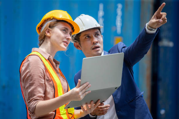 istock harbor worker woman and asian businessman using laptop computer checking list inventory loading Containers box at warehouse logistic in Cargo . import export shipping business. diversity teamwork 1319613363