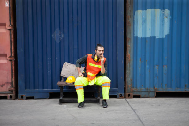 istock harbor worker take a break sitting and smoking cigarette on Containers box background at warehouse logistic in Cargo. 1319613467