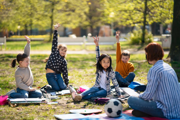istock Teacher with small children sitting outdoors in city park, learning group education concept. 1319613583