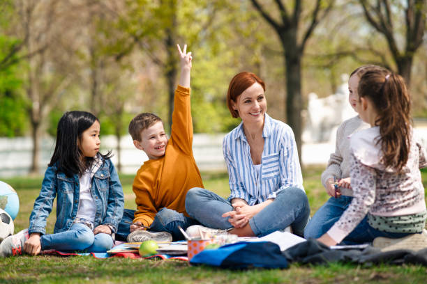 profesor con niños pequeños sentados al aire libre en el parque de la ciudad, concepto de educación grupal de aprendizaje. - educación en el hogar fotografías e imágenes de stock
