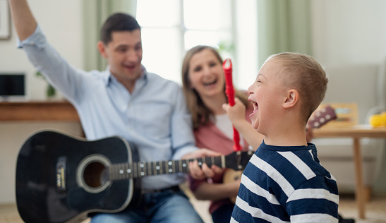 A cheerful down syndrome boy with parents playing musical instruments, laughing.