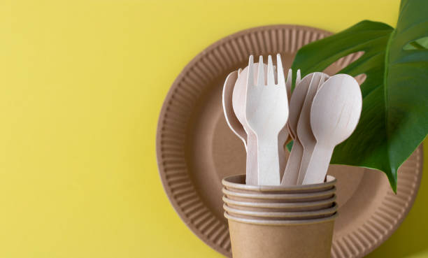 istock bunner environmentally friendly disposable tableware on a yellow background. Wooden forks and spoons in a paper cup with paper plate. Zero waste concept. Copy space. 1319614787