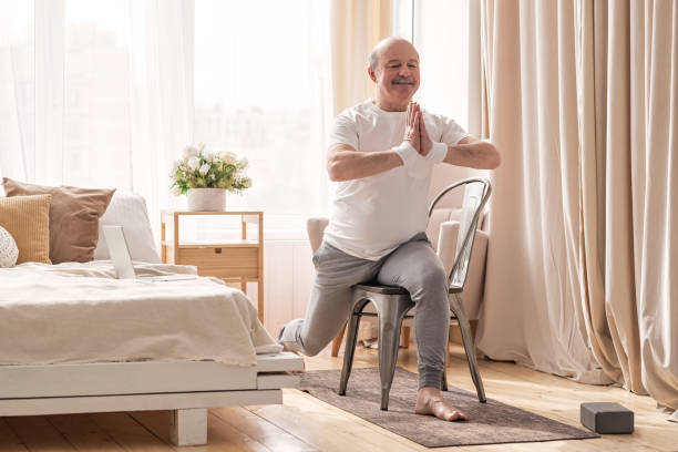 istock Elderly man practicing yoga asana warrior using chair 1319614895