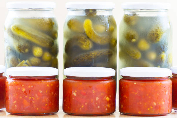 Glass jars filled with pickled cucumbers and tomato sauce against white background