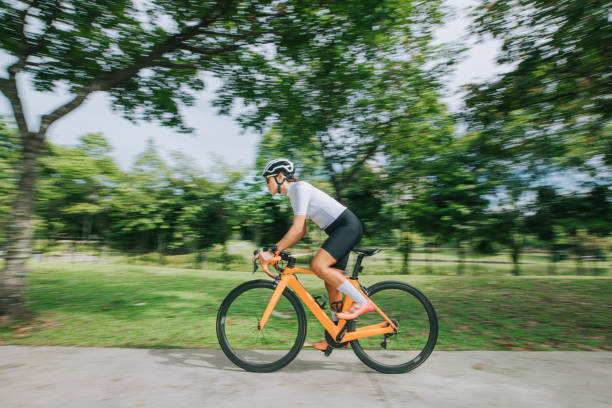 サイドビューアジアの中国の女性プロサイクリストアスリートスポーツマンは、公共の公園でサイクリングをスプリント - vitality blurred motion effort clothing ストックフォトと画像