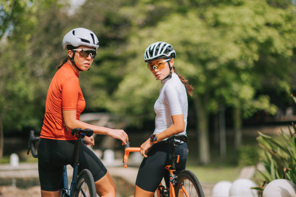 2 atleta ciclista professionista cinese asiatica che guarda indietro a cavallo nel parco pubblico - cyclist cycling road women foto e immagini stock