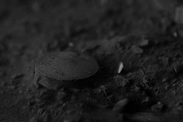 istock Activated charcoal black tablet pill on black coal powder background 1319626035