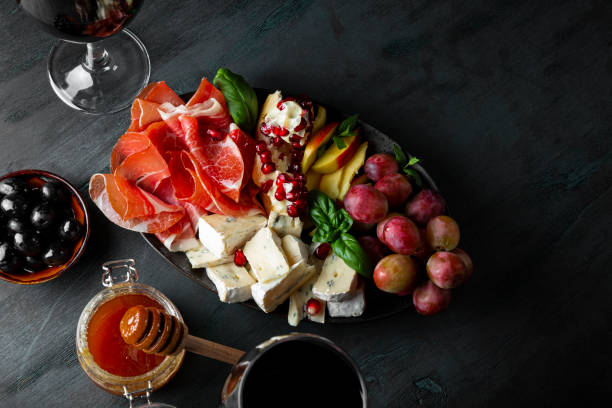 a set of appetizers for wine, jamon, pepperoni, cheese, grapes, peach and olives on a plate top view. snack board and two glasses of red wine on dark blue background, free space for text - italian cuisine wine food pasta imagens e fotografias de stock