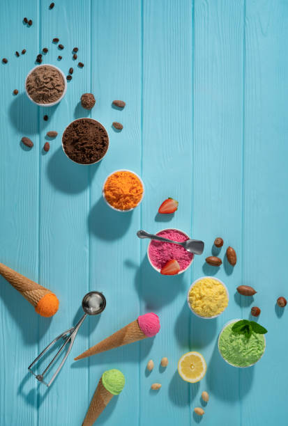 istock Assorted ice cream cups in a row and waffle cones colorful on blue wood background 1319628593