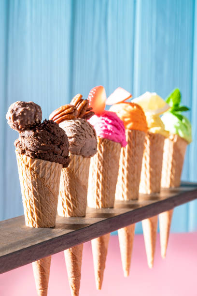 istock Assorted ice cream waffle cones in a row colorful different flavor on pink and blue wood 1319628721