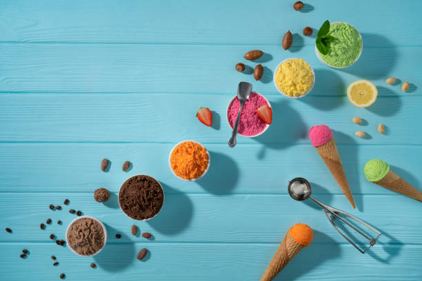 istock Assorted ice cream cups in a row and waffle cones colorful on blue wood background 1319628732