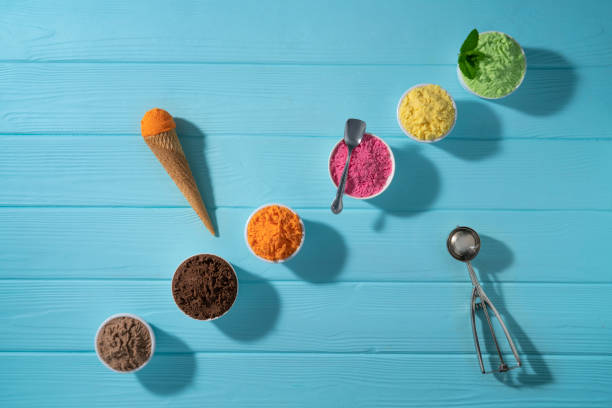 istock Assorted ice cream cups in a row and waffle cones colorful on blue wood background 1319628883