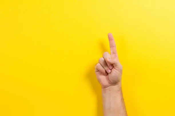 Man hand showing one finger on yellow background.