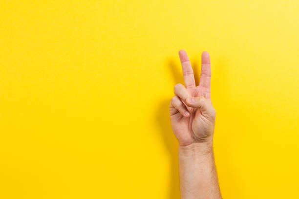 istock Man hand showing two fingers on yellow background. Number two symbol 1319634946
