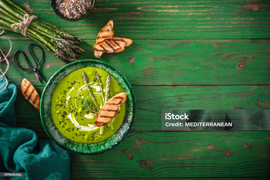 Asparagus soup plate with ingredients and bread toasts on green wood Asparagus soup plate with ingredients and bread toasts on green wooden table background Asparagus Stock Photo