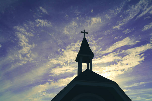 heavenly religious church chapel steeple in silhouette against a azure blue purple cloudscape sky stock photo