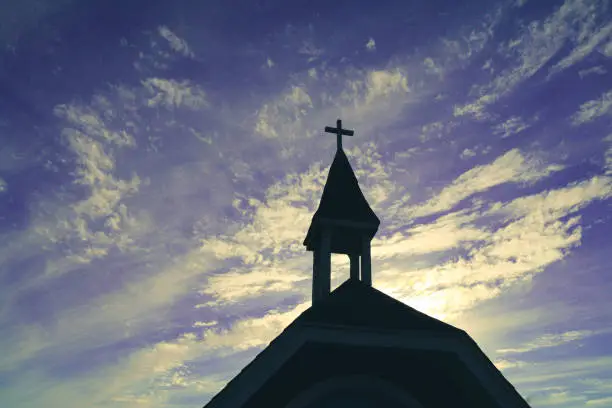 Photo of heavenly religious church chapel steeple in silhouette against a azure blue purple cloudscape sky