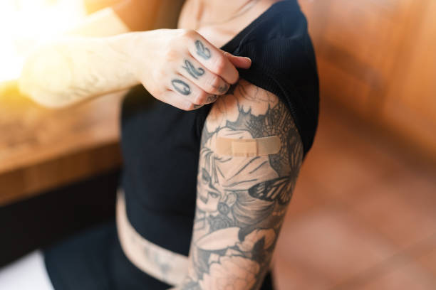 Tattooed woman with bandage from vaccine shot Woman with an adhesive bandage on the shoulder from getting the COVID-19 vaccine shot in the arm. tattoo arm stock pictures, royalty-free photos & images