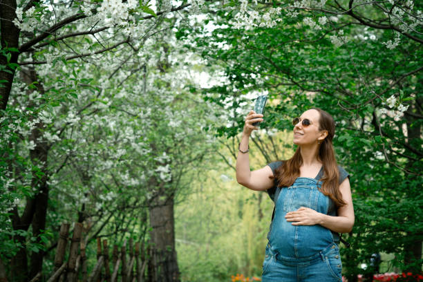 istock Pregnant woman making photos using smartphone in blooming park 1319637844