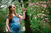 Pregnant woman making photos using smartphone in blooming park