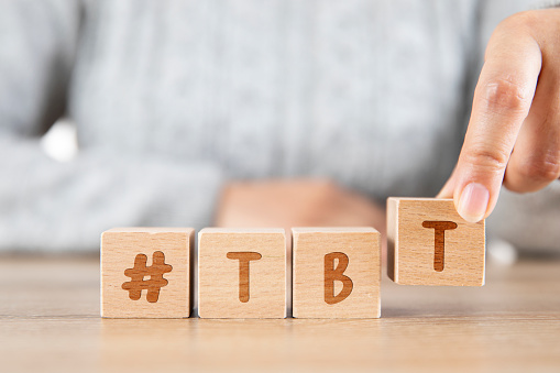 Wooden cubes with Hashtag tbt, meaning Throwback Thursday with woman writing it. Social media concept close-up