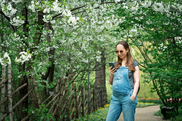 istock Pregnant woman making photos using smartphone in blooming park 1319638020