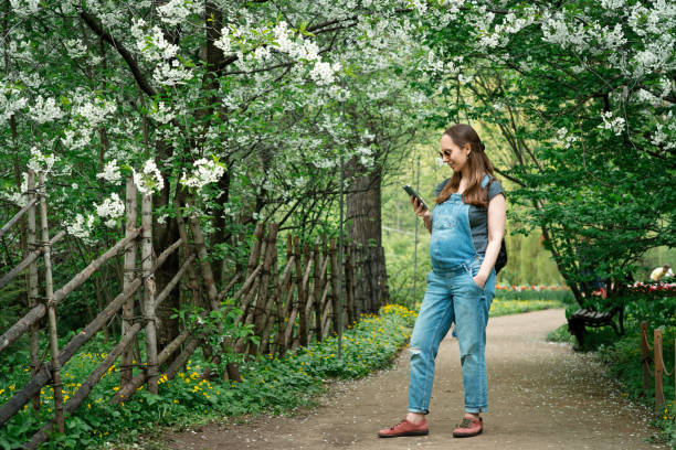 Pregnant woman making photos using smartphone in blooming park