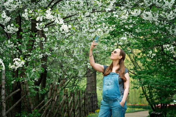 istock Pregnant woman making photos using smartphone in blooming park 1319638155