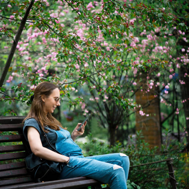 istock Pregnant woman using smartphone in blooming park 1319638273