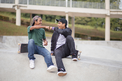 Asian skateboarders sitting taking a break and talking at skateboard park