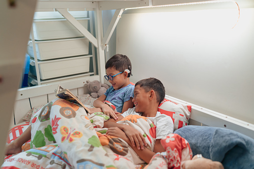 Asian boy with cochlear implant reading with his brother in bed