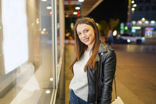 istock Young woman standing next to store window on sidewalk and looking at camera 1319641864