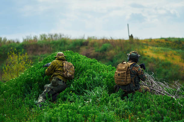 вид со спины страйкбольных игроков, сидящих в засаде - hunting two people camouflage rifle стоковые фото и изображения