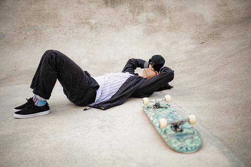 Asian skateboarder taking rest in the public skateboarding park during weekend