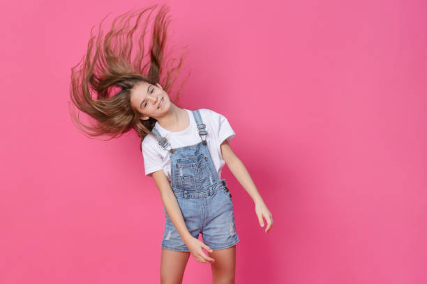 ragazza bianca di 10 anni in un top bianco che sventola capelli lunghi, divertendosi su uno sfondo rosa, emozioni, bambino - 10 11 years cheerful happiness fun foto e immagini stock