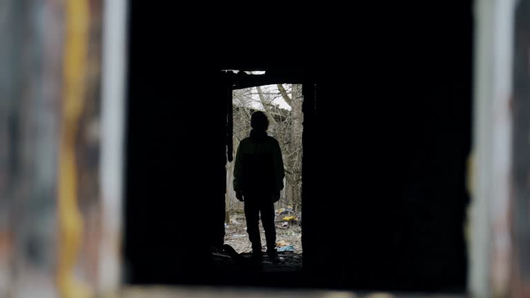 The boy goes into an abandoned burned-out house and looks around. Cool shooting through the window. Textured silhouette of a boy