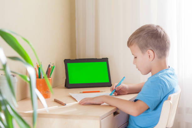 istock Smart school boy drawing picture, tablet with green screen stay on desk 1319651878