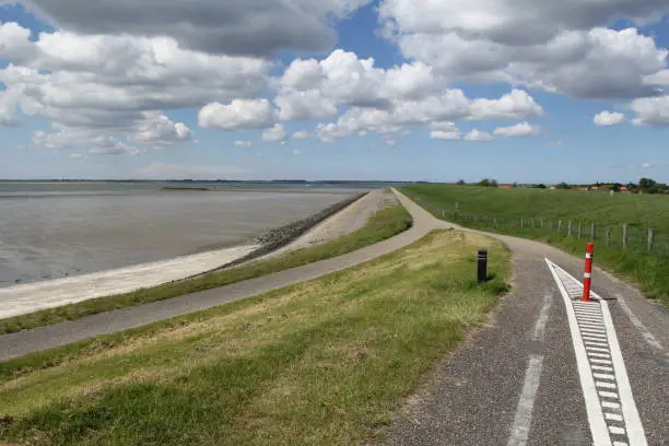 a road at the seawall with a beautiful view at scheldt river with mudflats with eb and a blue sky with clouds in springtime