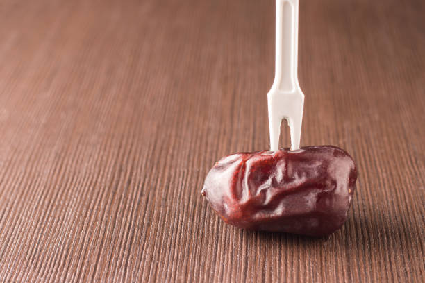 istock Single date fruit on a wooden table with a stuck fork 1319657544