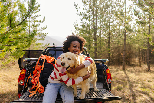 Photo of young smiling woman on a road trip with her best friend, her retriever dog, riding along on their pick up truck