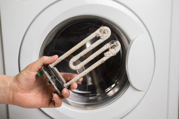 una persona sostiene en su mano un elemento de calefacción eléctrica dañado de la lavadora. trabajos de reparación y restauración - faulty fotografías e imágenes de stock