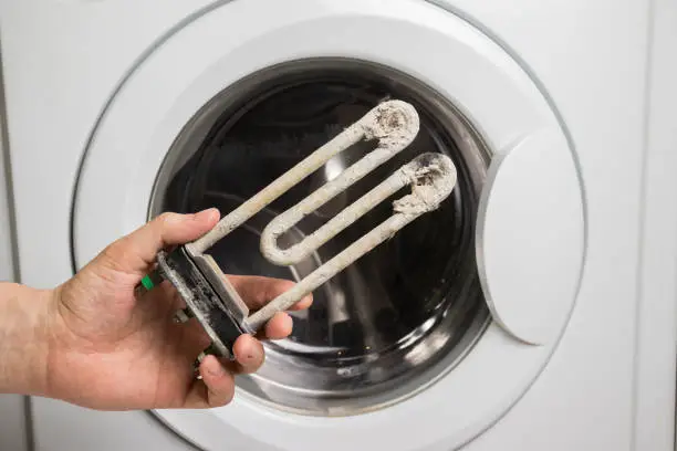 Photo of A person holds in his hand a damaged electric heating element from the washing machine. Repair and restoration work