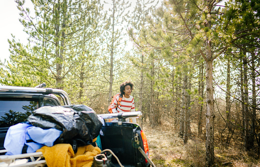 Photo of young smiling woman on a road trip, setting up a camp on a great spot she's found in the woods