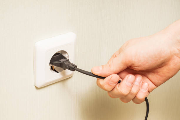 la mano de una persona tira de un cable eléctrico conectado a una toma de corriente - electric plug outlet pulling electricity fotografías e imágenes de stock