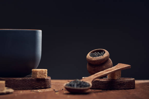 sucha herbata w drewnianych łyżkach i w drewnianym słoikui kawałki cukru trzcinowego na stole, na ciemnym tle. - dry tea zdjęcia i obrazy z banku zdjęć
