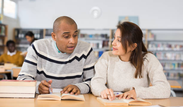 istock Positive hispanic man and woman reading books in library 1319661552