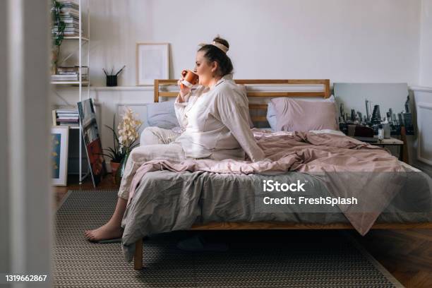 Plus Size Woman Sitting On Her Bed And Drinking Tea Stock Photo - Download Image Now