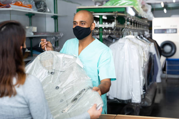 istock Male employee in protective mask with client in modern laundry, returning clothing after cleaning 1319664034