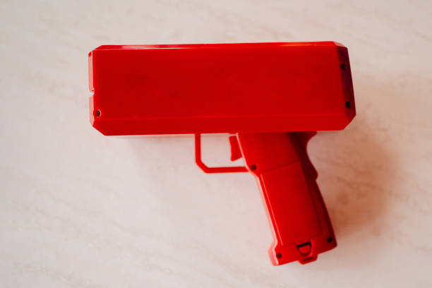ярко-красный пистолет, который стреляет деньгами. - guns and money стоковые фото и изображения