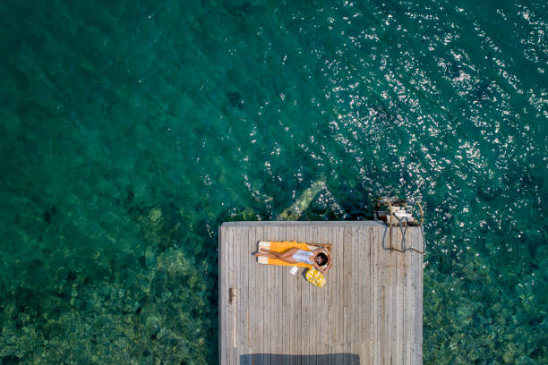 Beautiful woman sunbathing alone on a wooden pier in sea aerial photo Aegean sea Muğla - Turkey chaise longue woman stock pictures, royalty-free photos & images